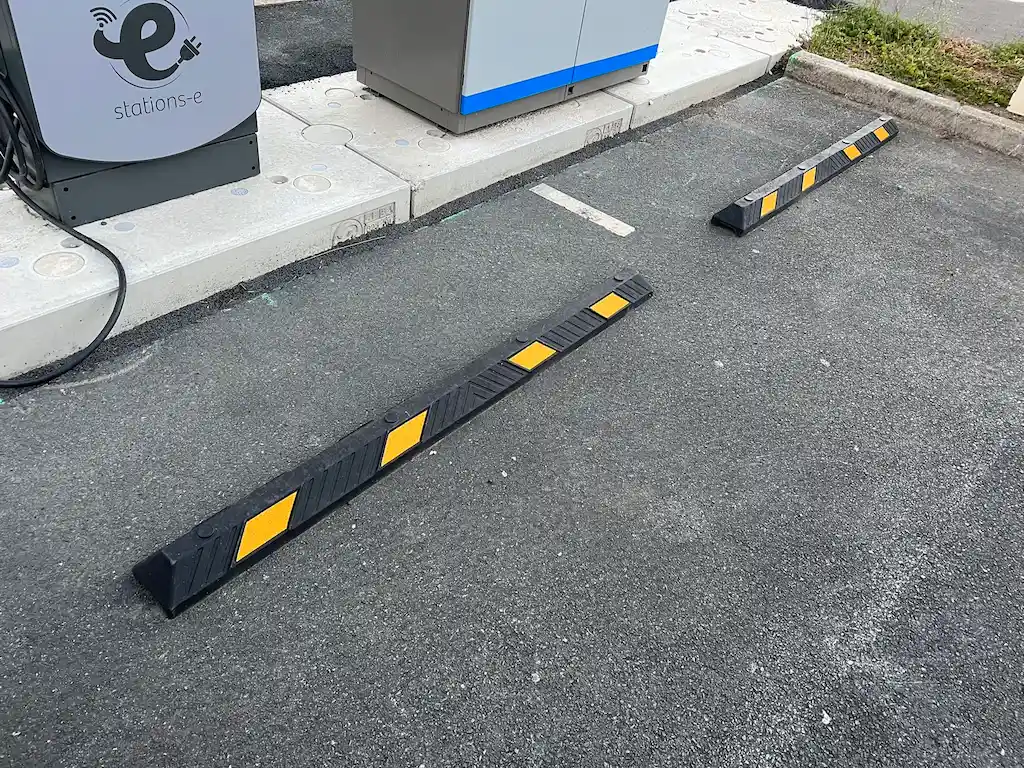 Two black and yellow parking curbs are installed in front of the EV charging station to assist with parking and protect the charging station.
