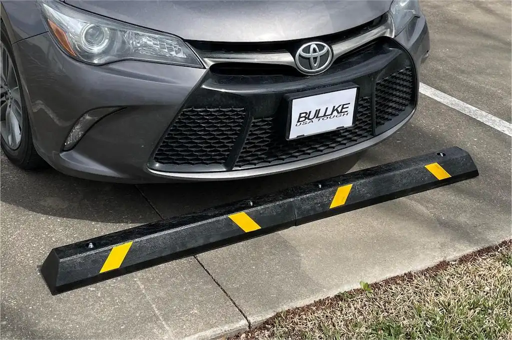 A gray car is parked behind a black and yellow car parking stopper.