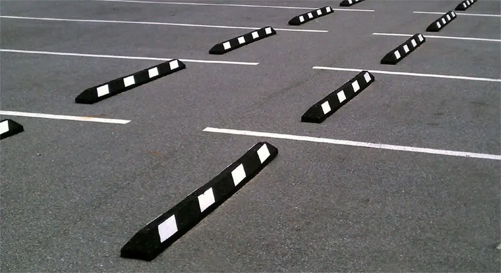 Black and white rubber wheel stops installed in a parking lot.